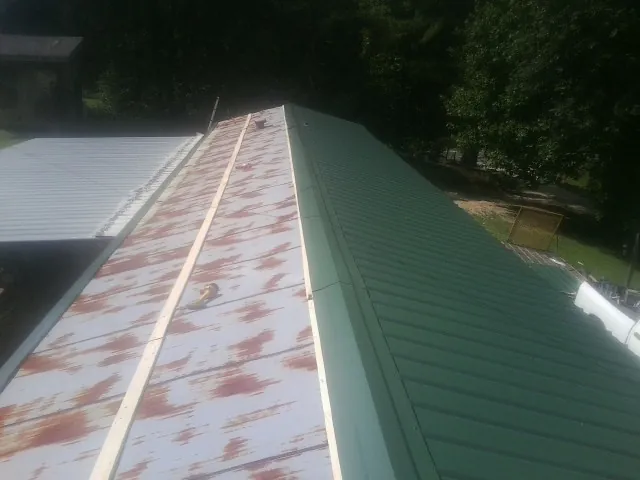 Old rusted panels beside newly installed green metal roofing — Wind Damage Roof Repair by Roofing Brothers in Paradise