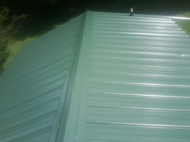 New green metal panels meeting at the ridge of a roof — Flat Roof Repair work by our crew in Paradise