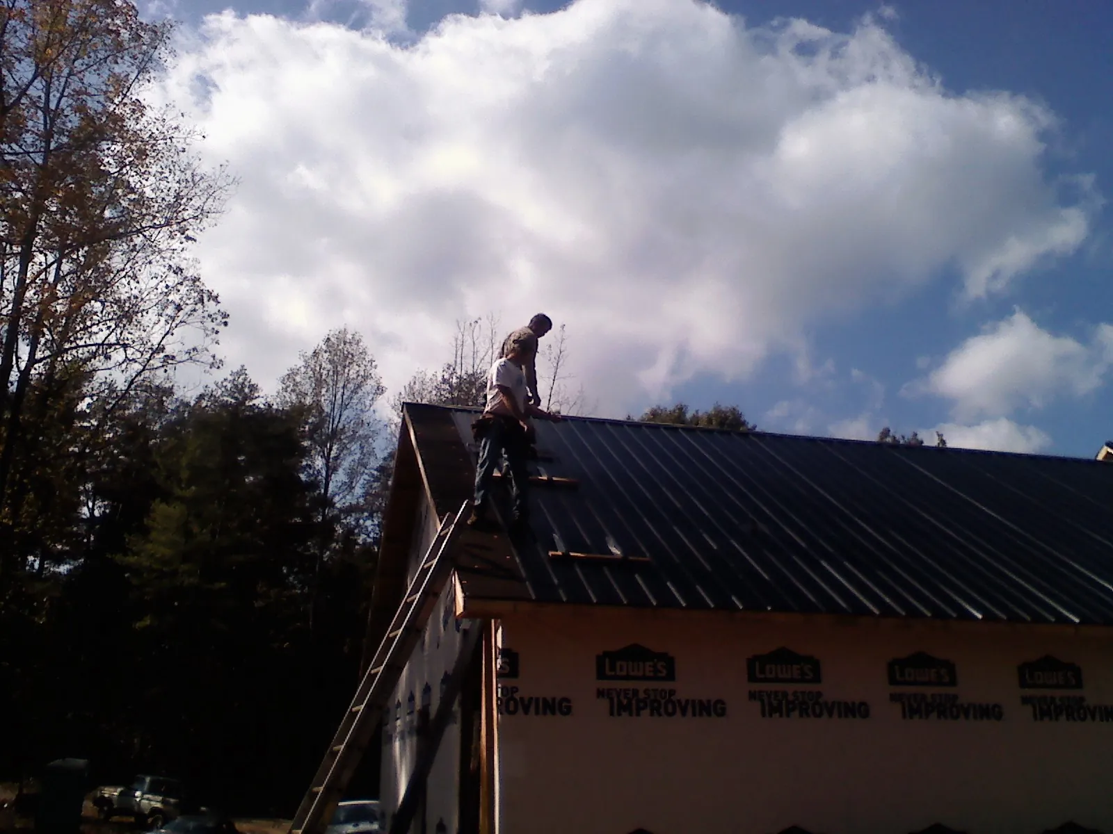 Roofer fastening dark metal panels high against a cloudy sky, from a Roof Inspection job in Paradise