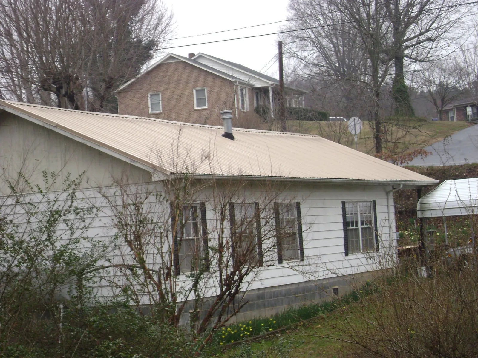 Tan metal roof on a white sided house set into a hillside — Commercial Roofing by Roofing Brothers in Paradise
