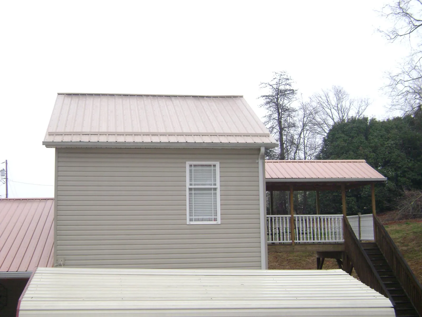 Tan metal roofs on a two story addition and attached porch, from a Roof Replacement job in Paradise